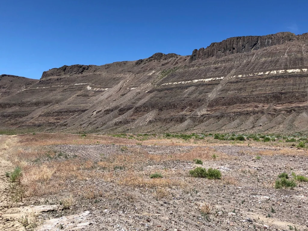 Dramatic layered rock formations rise against a clear blue sky, showcasing geological features in a dry landscape. Ideal for geology enthusiasts.